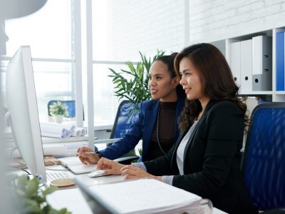 Smiling Filipino business women working on computer togetehr